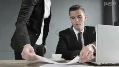 穿着黑色西装的<strong>年轻商人</strong>在办公室用笔记本电脑给他的同事提供财务数据图表